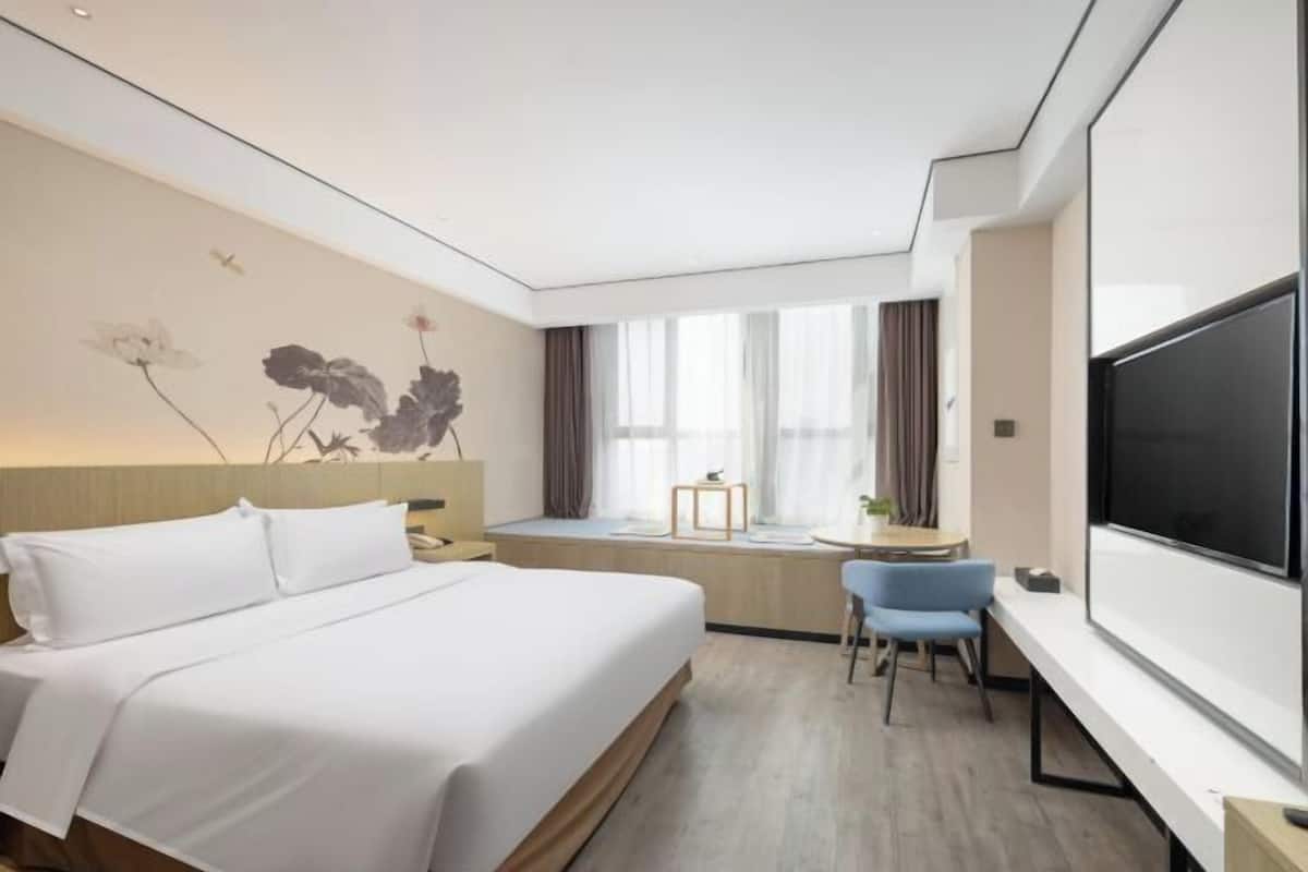 A hotel room with a bed, a desk, a chair, a TV, and a window with curtains.