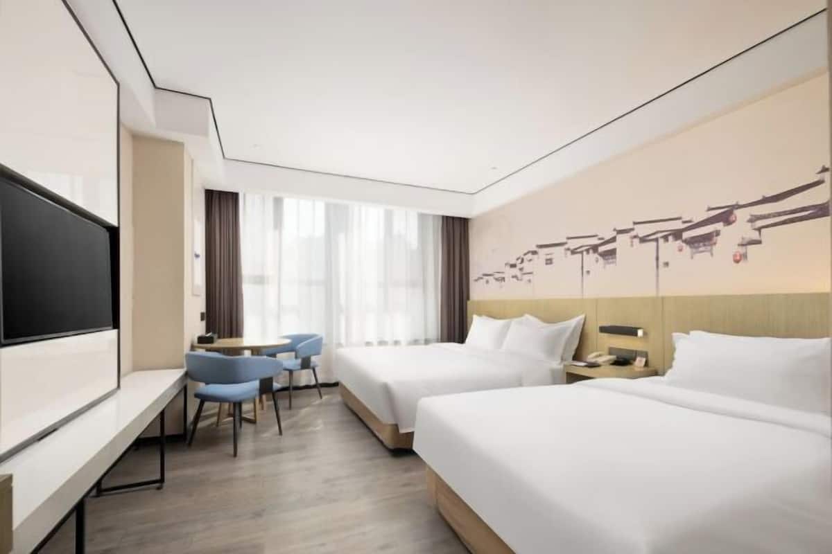 A hotel room with two beds, a TV, a desk, and a chair.