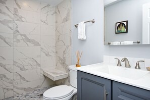 Ein Badezimmer mit Marmorfliesen, einer weißen Toilette, einem Waschbecken mit zwei Wasserhähnen und einem Handtuchhalter mit einem Handtuch.