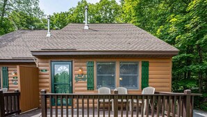 Een chalet met een veranda, groene luiken en een welkomstbord.