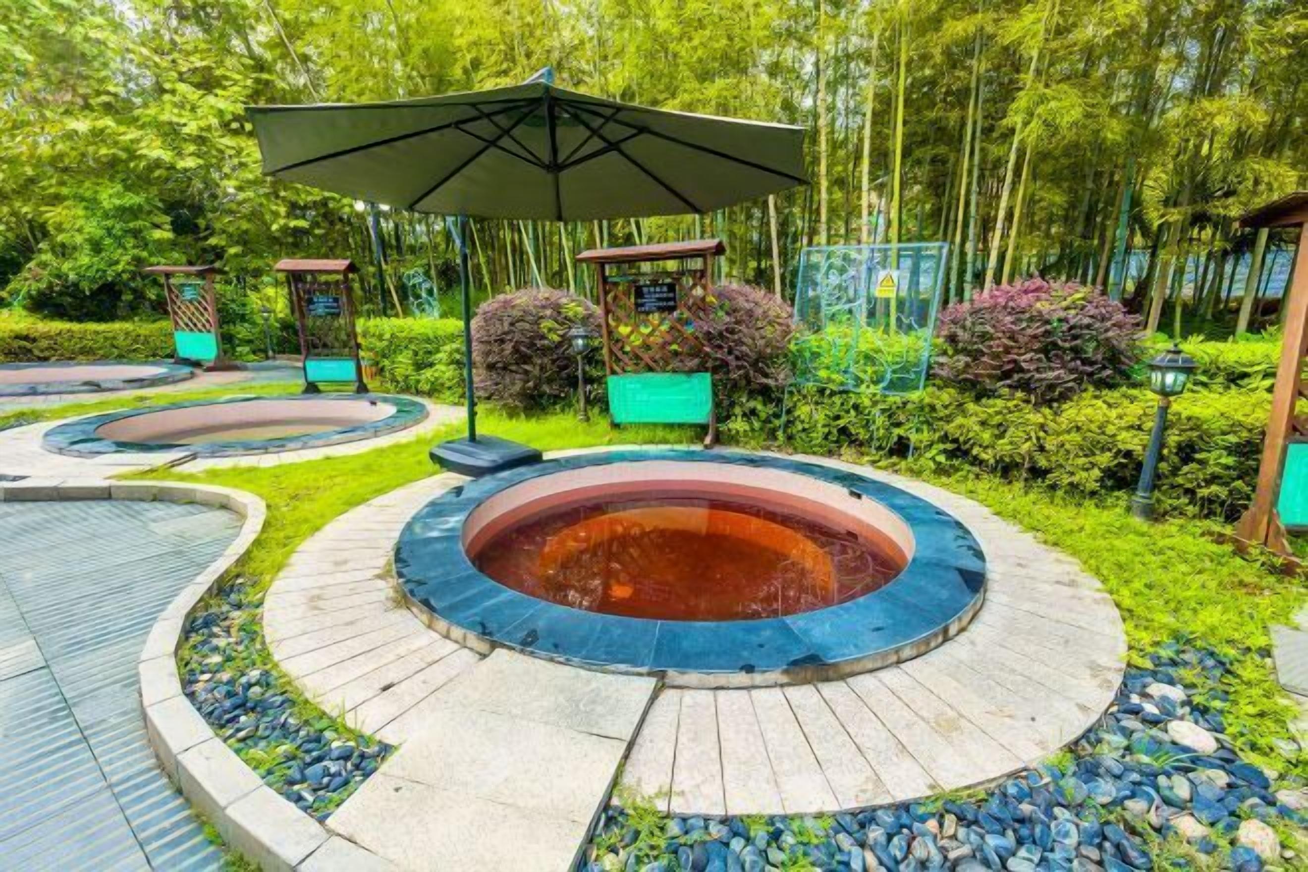 A circular hot tub area with a surrounding stone path, surrounded by lush greenery and a gazebo.