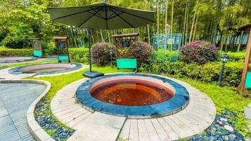 A circular hot tub area with a surrounding stone path, surrounded by lush greenery and a gazebo.