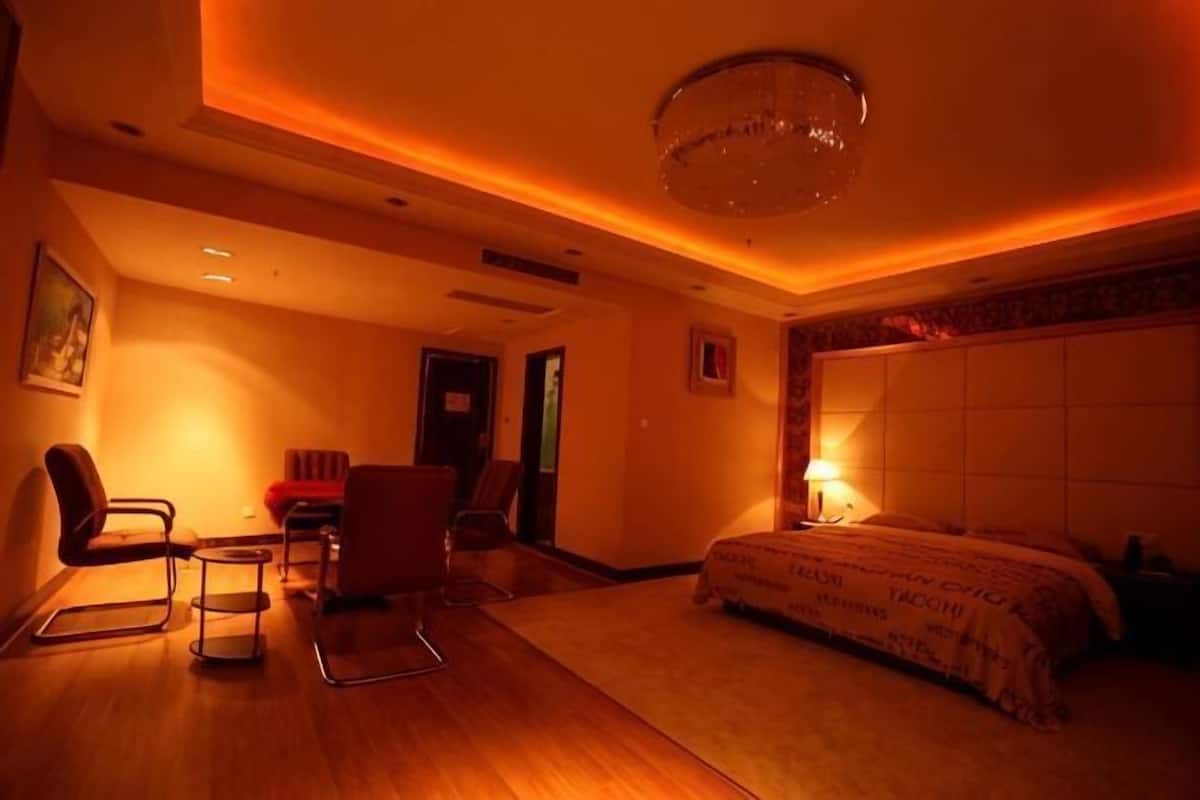 A hotel room with a bed, a desk, two chairs, a small table, and a chandelier.
