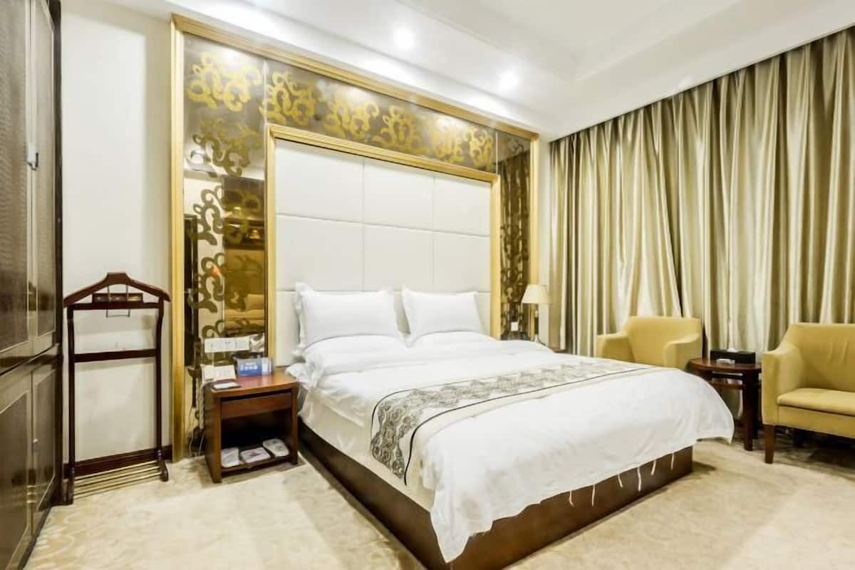 A hotel room with a large bed, a wooden nightstand, a chair, and a curtain.