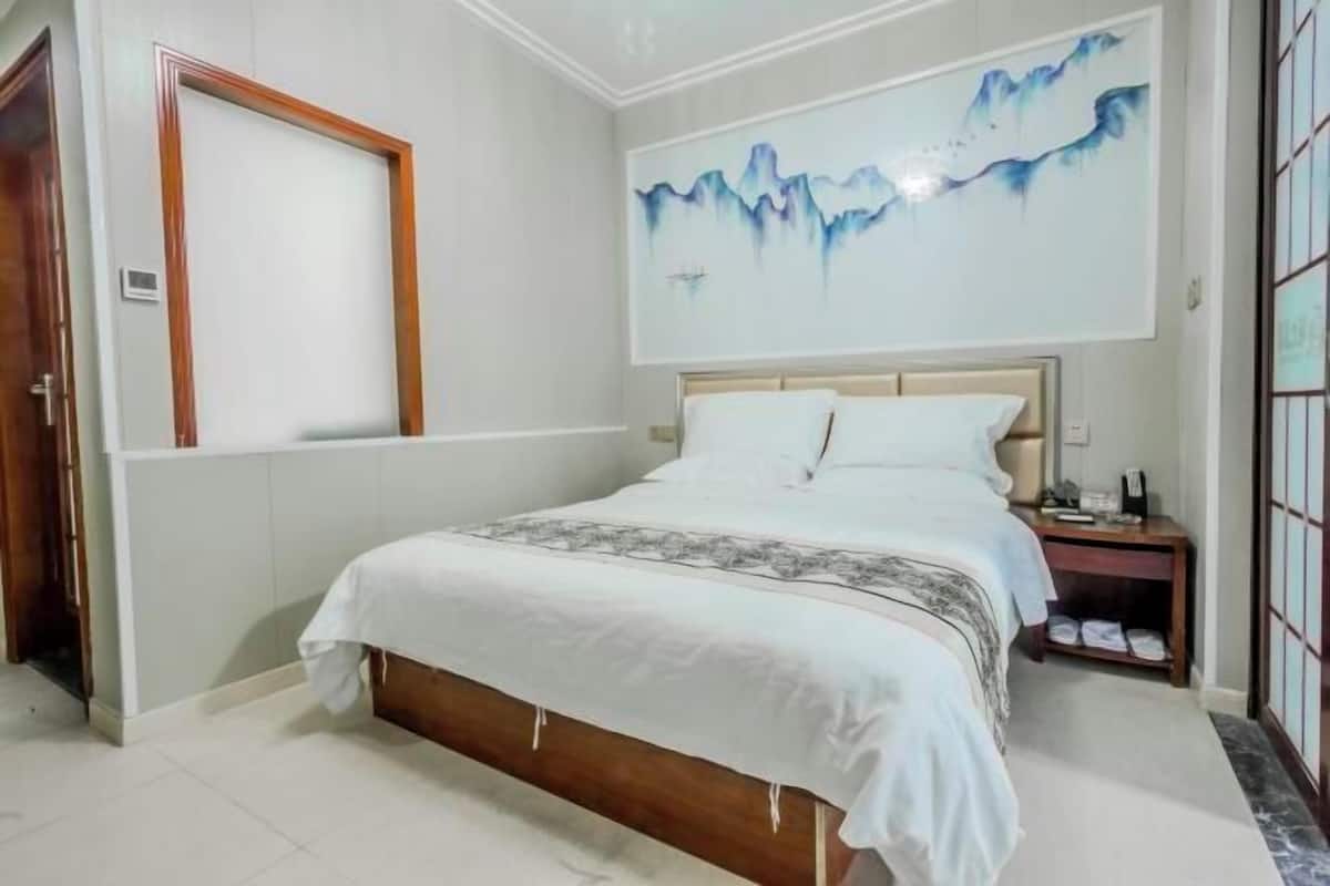 A bedroom with a bed, a nightstand, a wall-mounted painting, and a door.