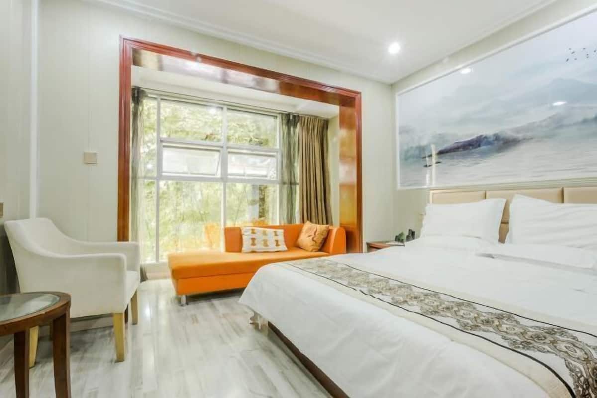 A hotel room with a large bed, a window with curtains, a sofa, and a chair.