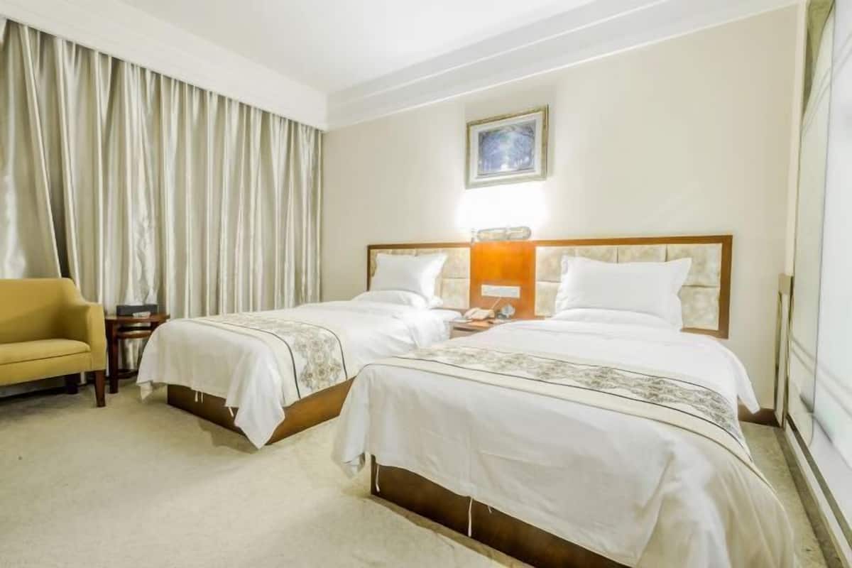 A hotel room with two single beds, a sofa, a bedside table, a lamp, and a window with curtains.