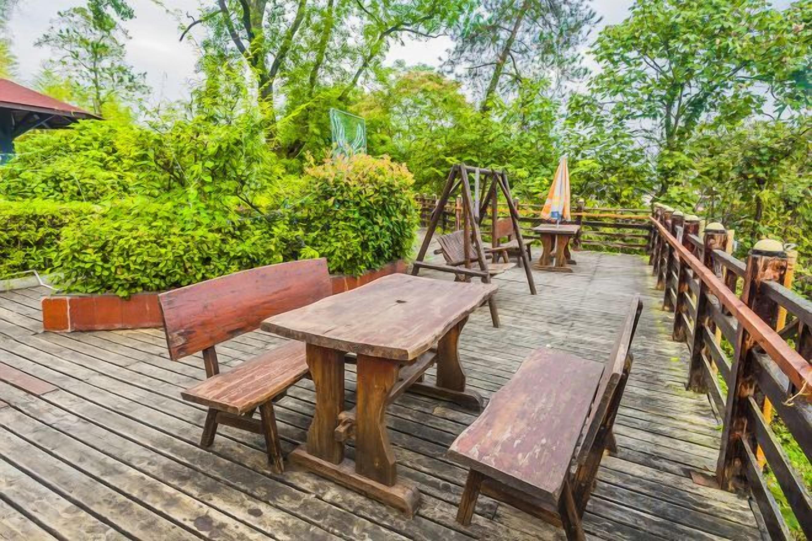 A wooden deck with benches and tables, surrounded by greenery.