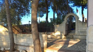 A stone pathway leading to a gated entrance, surrounded by trees and a clear sky. - VIILLA PAOLA 4 beds, private garden in the Residence Villa Carla (Vieste)
