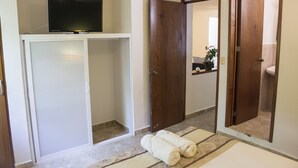 Een hotelkamer met een televisie op een kast, een kledingkast, een spiegel en een bed met opgerolde handdoeken.