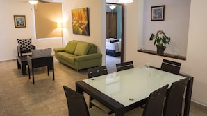 Een moderne woonkamer met een eettafel met glazen blad, een groene bank en een plafondventilator.
