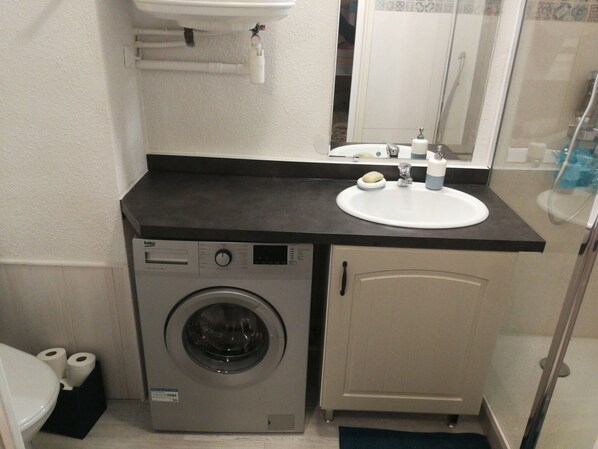 A compact bathroom with a washing machine, a sink, and a toilet.