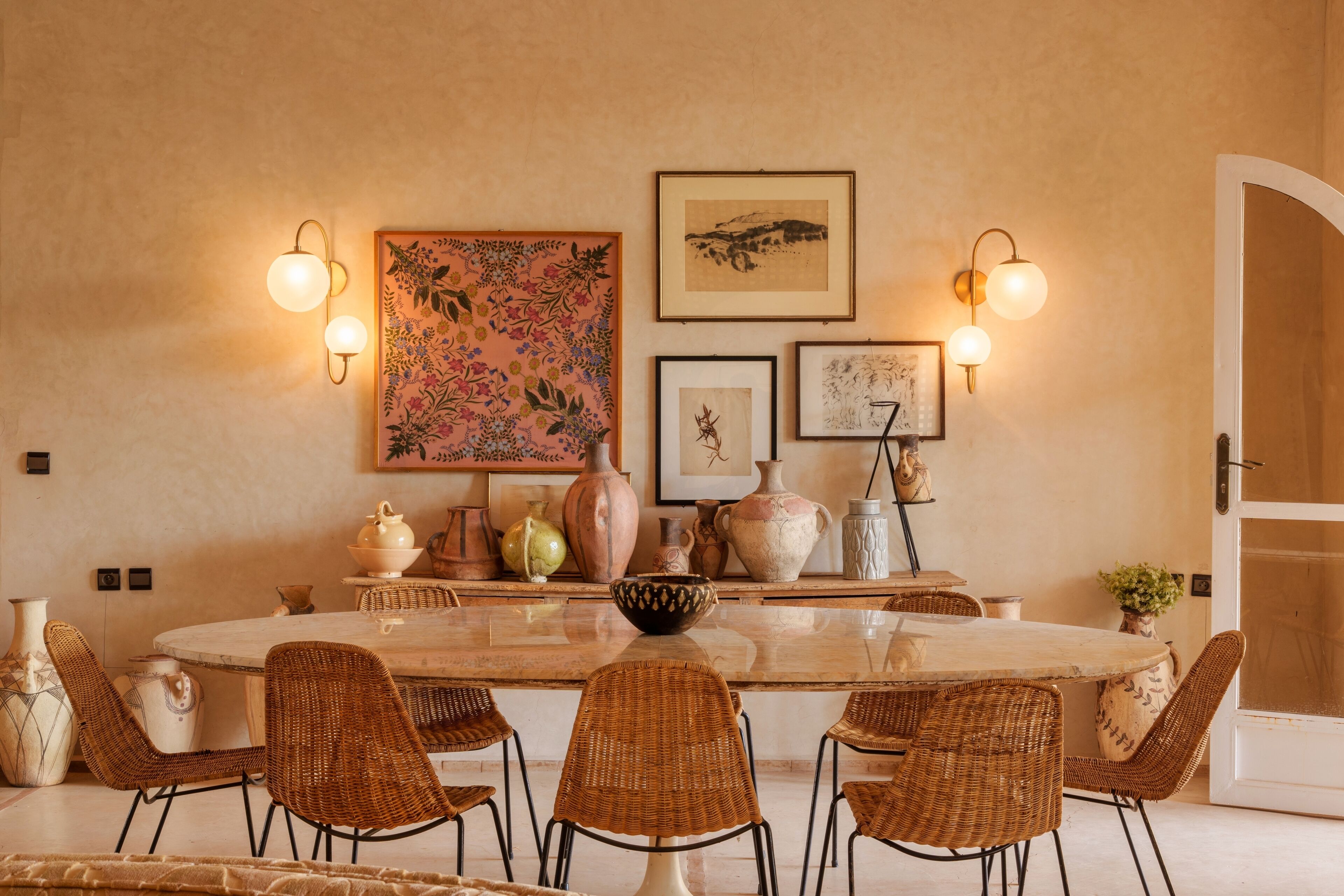 A dining area with a round table, wicker chairs, wall-mounted light fixtures, and various decorative items.