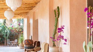 A covered outdoor area with a wooden ceiling, potted plants, and a seating area with a sofa and chairs. - The Gardener's House (Aghouatim)