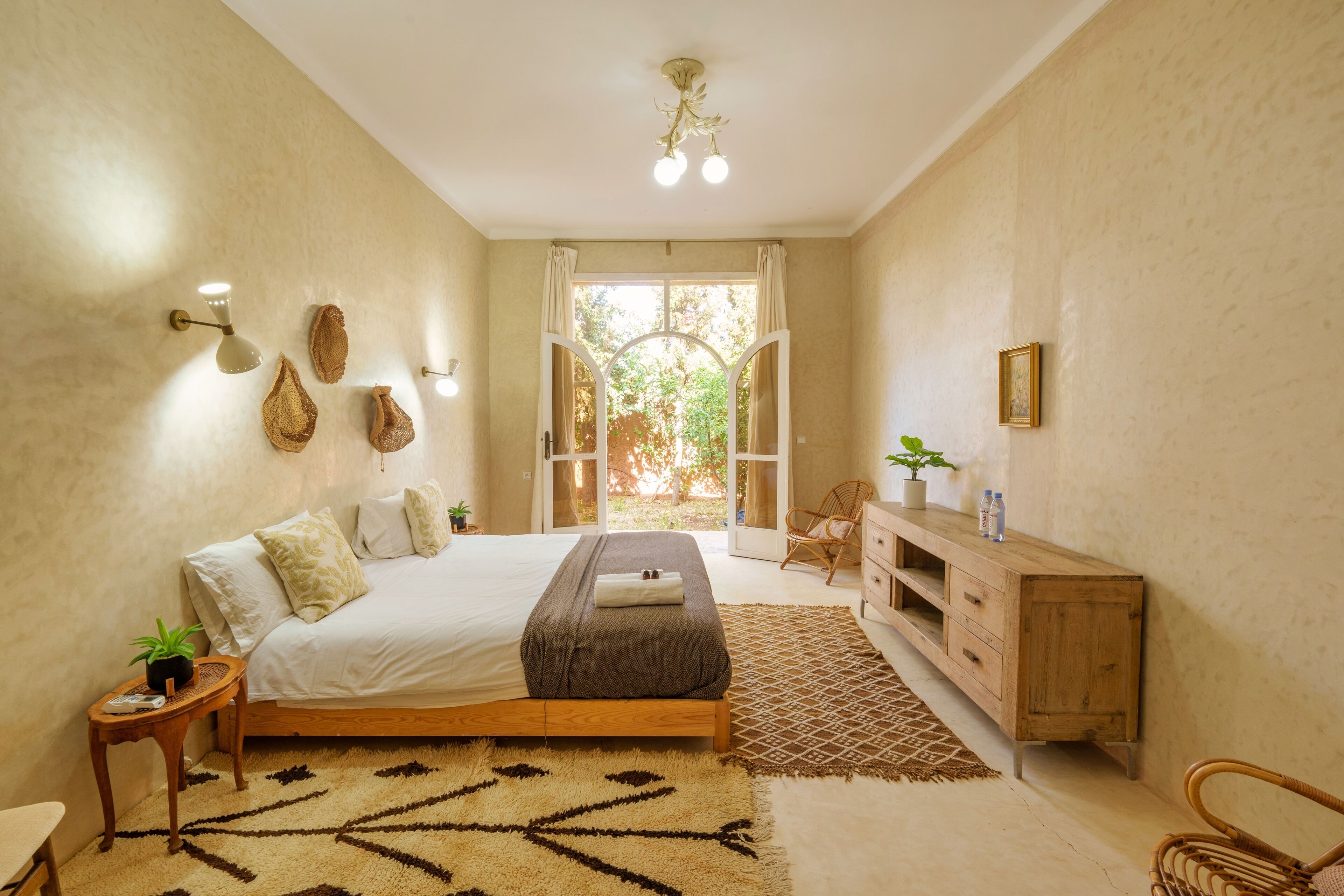 A bedroom with a bed, bedside tables, a wooden cabinet, a patterned rug, and a view of the outdoors.