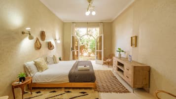 A bedroom with a bed, bedside tables, a wooden cabinet, a patterned rug, and a view of the outdoors.