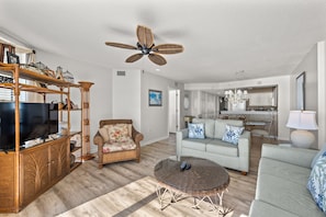 A spacious living room with a television, wicker furniture, and a ceiling fan.