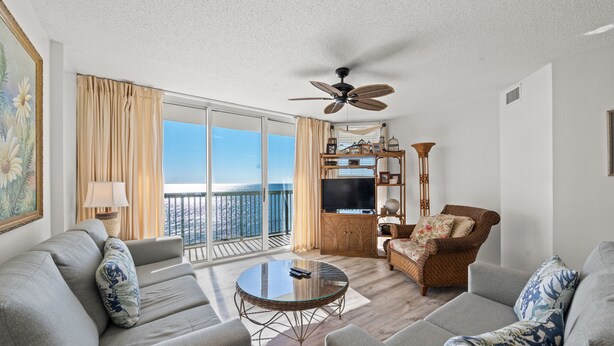 A spacious living area with a balcony, a television, and a ceiling fan. - Spacious Oceanfront condo, great amenities + Free Attraction Tickets! (North Myrtle Beach)