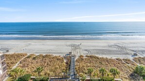 A beach view with a boardwalk leading to a lifeguard tower, sandy beach, and ocean. - Spacious Oceanfront condo, great amenities + Free Attraction Tickets! (North Myrtle Beach)