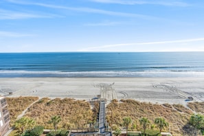 A beach view with a boardwalk leading to a lifeguard tower, sandy beach, and ocean.