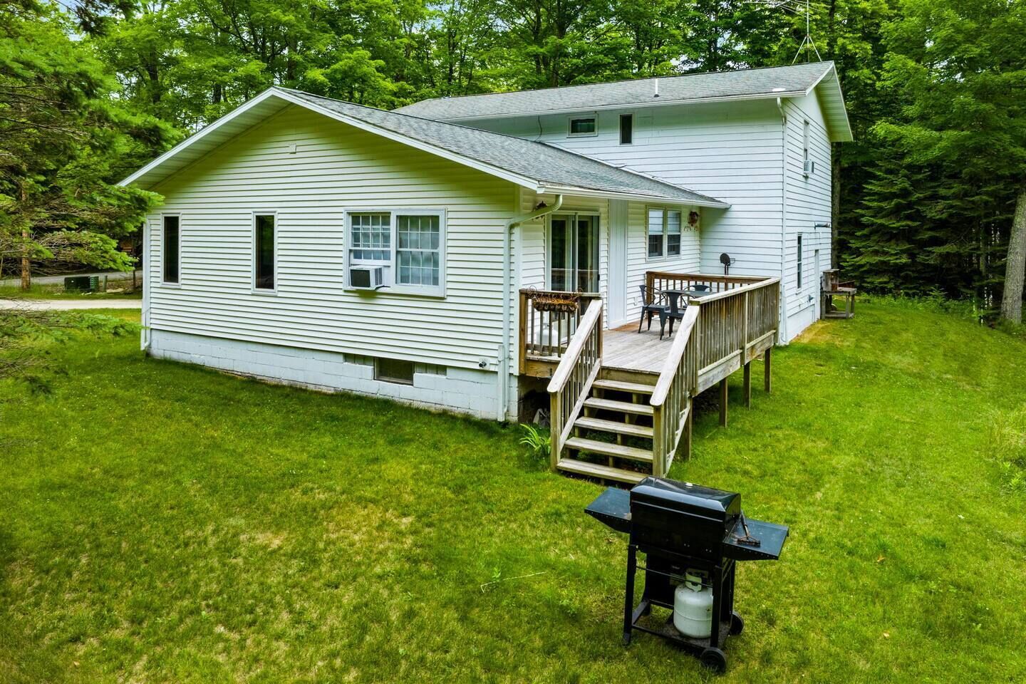 A two-story house with a deck and a barbecue grill in the yard.