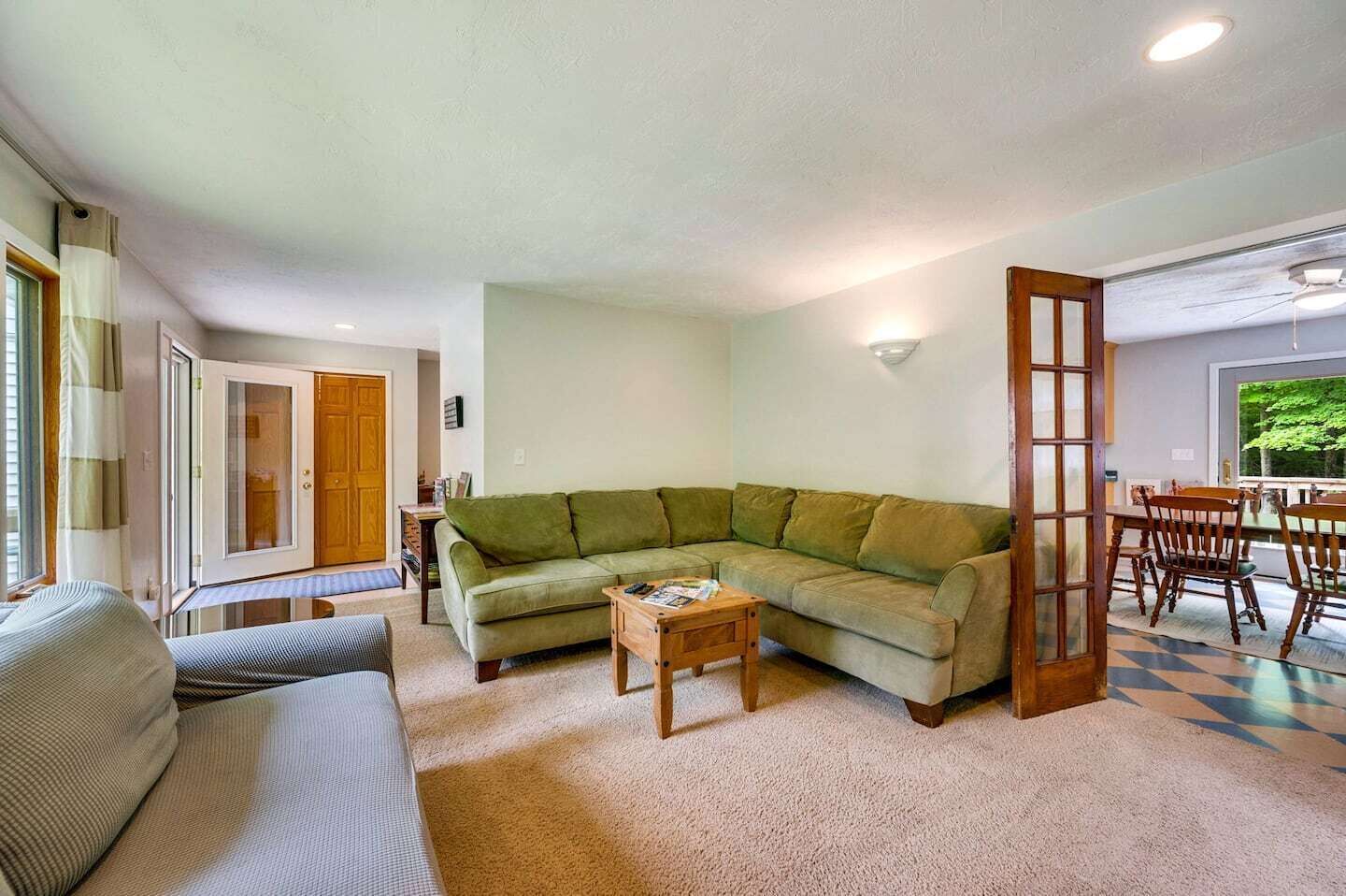 Un salon avec un canapé d’angle vert, une table basse en bois et un coin repas comprenant une table et des chaises.