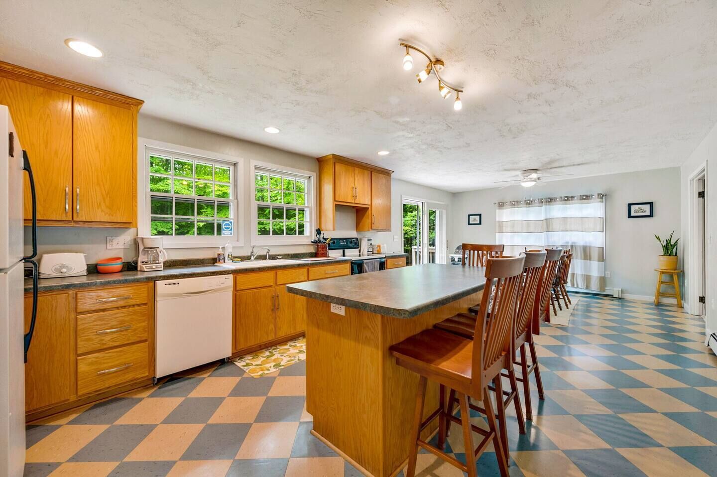 Una cocina con armarios de madera, una isla central con taburetes de bar, un lavavajillas y una cafetera.