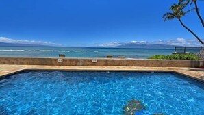 A swimming pool with clear blue water, a view of the ocean, and a palm tree. - Corner condo with direct beach access (Lahaina)