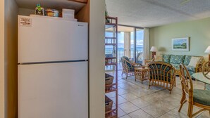 A compact kitchen with a refrigerator and a dining area with wicker furniture and a view of the outdoors. - Corner condo with direct beach access (Lahaina)