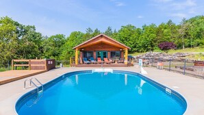 A swimming pool with a wooden deck and lounge chairs, surrounded by a wooden cabin with a covered patio. - Sleeps 16-Marina, Pool, Roaring River & Table Rock (Cassville)