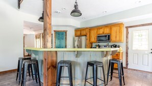 A kitchen with wooden cabinets, a central island with stools, a refrigerator, and a microwave. - Sleeps 16-Marina, Pool, Roaring River & Table Rock (Cassville)