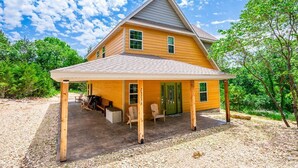 A two-story wooden house with a covered porch, a green door, and a gravel driveway. - Sleeps 16-Marina, Pool, Roaring River & Table Rock (Cassville)