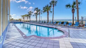 A swimming pool with blue water, surrounded by palm trees and blue lounge chairs. - Gulf Front Beauty - Beach Service for 2- Owner Managed (Panama City Beach)