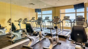 A gym with various exercise machines, large windows, and a mirror wall. - Gulf Front Beauty - Beach Service for 2- Owner Managed (Panama City Beach)