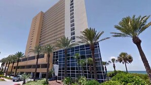 A tall hotel with a modern design, featuring a mix of glass and beige exterior, surrounded by palm trees and a clear sky. - Gulf Front Beauty - Beach Service for 2- Owner Managed (Panama City Beach)
