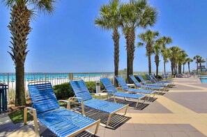Eine Strandlounge mit Reihen blauer Liegestühle, Palmen und freiem Blick auf das Meer.