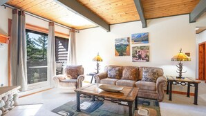 Sala de estar con sofá, mesa de centro y lámparas. Cuenta con un ventanal corredero que da a un espacio al aire libre.