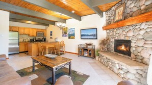 Amplia sala de estar con chimenea de piedra, techo de madera y cocina con armarios de madera.