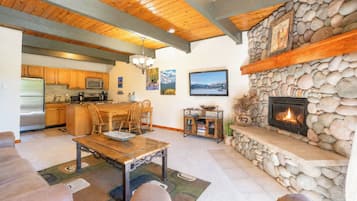 Amplia sala de estar con chimenea de piedra, techo de madera y cocina con armarios de madera.
