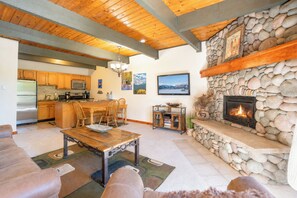 A spacious living area with a stone fireplace, wooden ceiling, and a kitchen with wooden cabinets. - Sundowner Last Run Condo: Ski-In, 2 Blocks To Main St (Breckenridge)