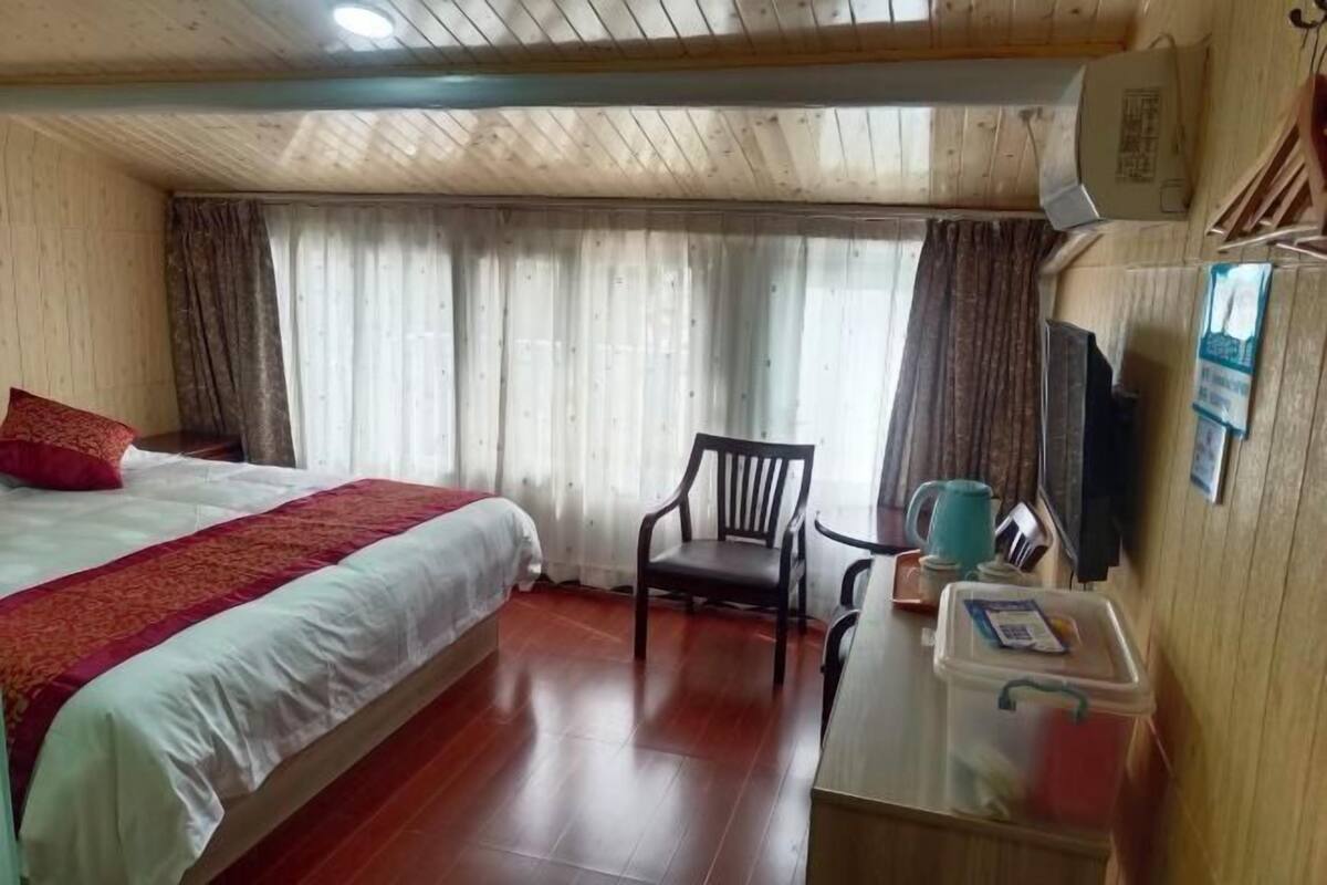 Una habitación de hotel con cama, una silla, un escritorio con una taza y una ventana con cortinas.