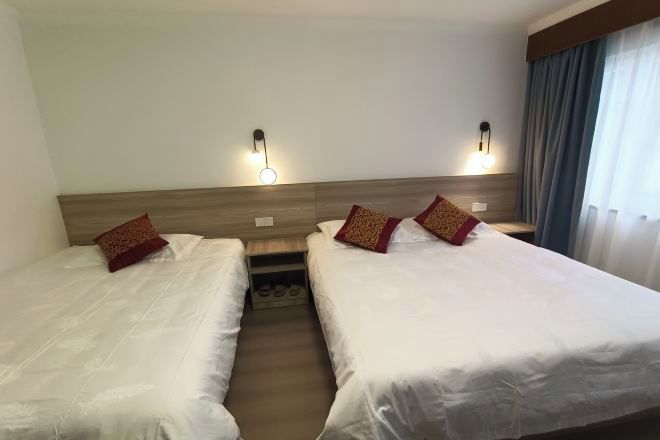 A hotel room with two single beds, each with a pillow and a nightstand.