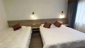 A hotel room with two single beds, each with a pillow and a nightstand.
