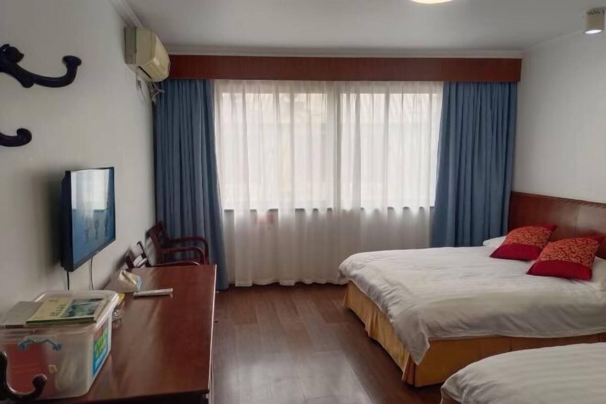 Una habitación de hotel con cama, escritorio, televisión y ventana con cortinas.