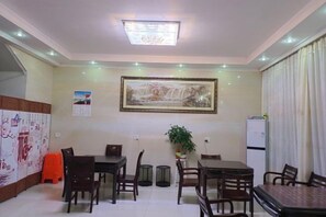A dining area with a table and chairs, a ceiling light, a framed picture on the wall, and a refrigerator. - Jinmalou Hotel (Yueqing)