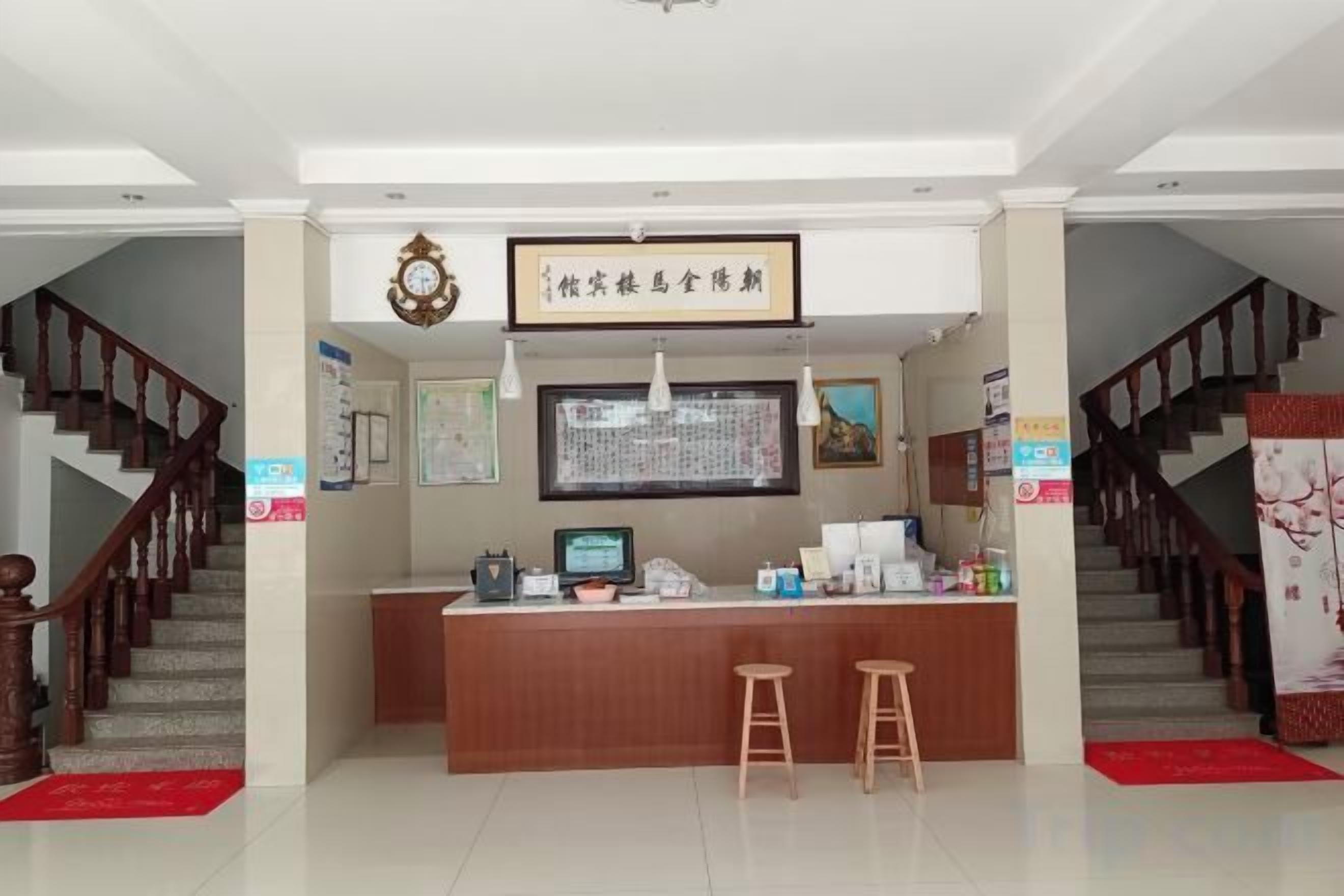 A reception area with a wooden counter, two stools, a framed sign, a computer monitor, and a staircase.