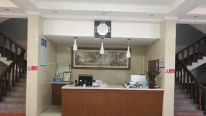 A reception desk with a clock, framed artwork, and a potted plant. - Jinmalou Hotel (Yueqing)