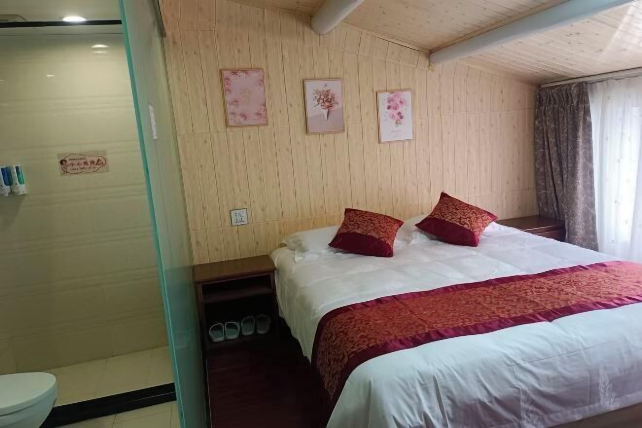 A hotel room with a bed, a shower, and a wooden wall with framed pictures.