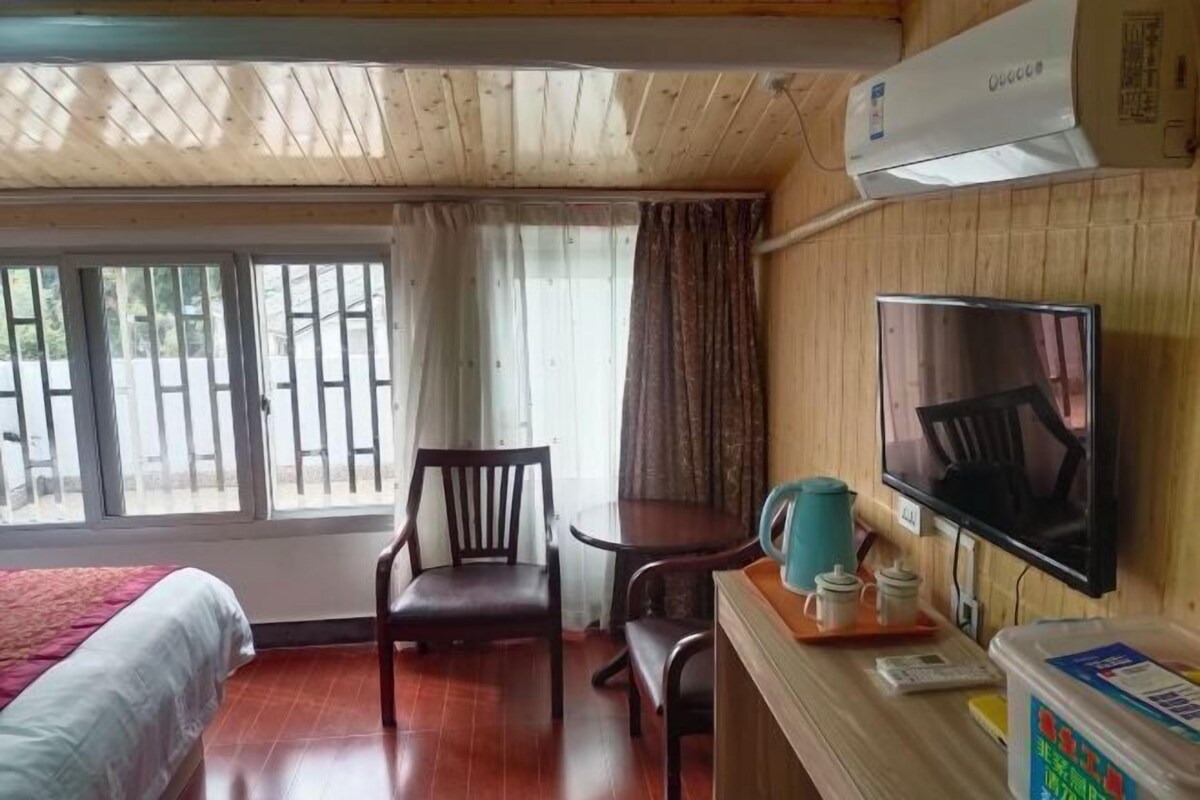 Ein Zimmer mit einem Bett, einem Schreibtisch mit Fernseher, einem Sessel und einem Fenster mit Vorhängen.