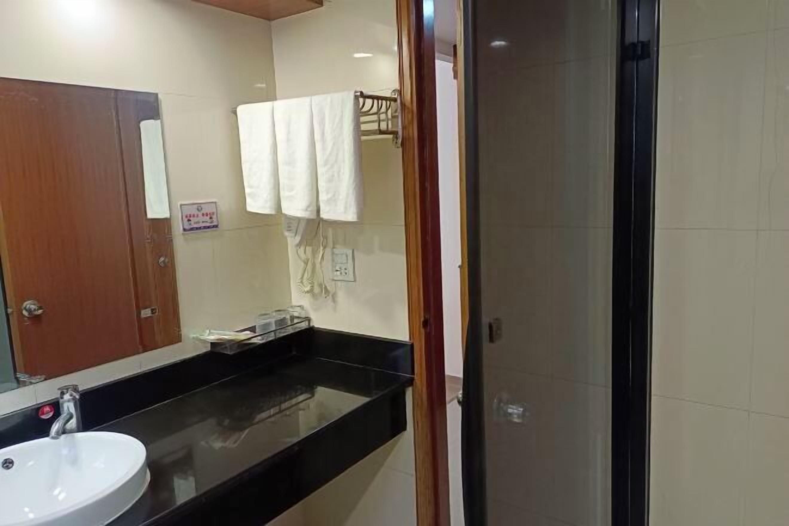 A bathroom with a black countertop, a white sink, a towel rack, and a wooden door.